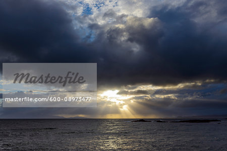 Sun shining through the storm clouds at sunrise along the Scottish coast at Mallaig in Scotland, United Kingdom