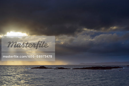 Sun shining through the storm clouds at sunrise along the Scottish coast at Mallaig in Scotland, United Kingdom