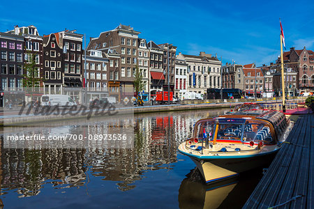 Typical buildings line the street with a tour boat moored along the seawall of the Oudezijds Voorburgwal canal in Amsterdam, Holland