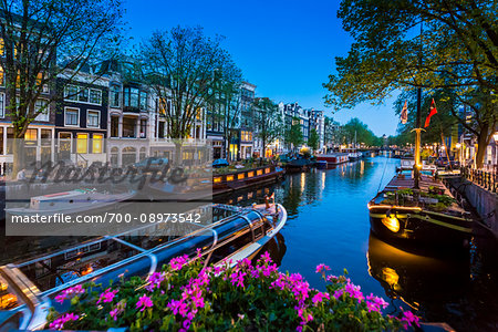 Tour boat travelling along the canal with houseboats moored along the seawall of the Keizersgracht in the enveing in Amsterdam, Holland.