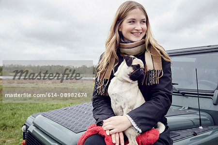 Young woman sitting on off road vehicle in field with dog on lap