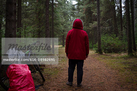 Rear view of male mountain biker in red parka looking out at forest