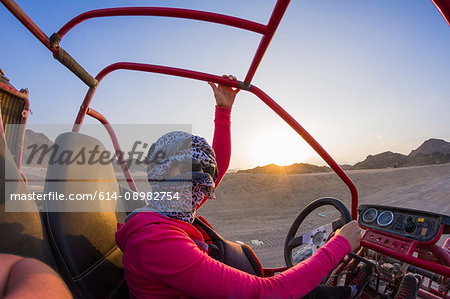 Young woman with head wrapped in scarf driving beach buggy in desert, Hurghada, Al Bahr al Ahmar, Egypt