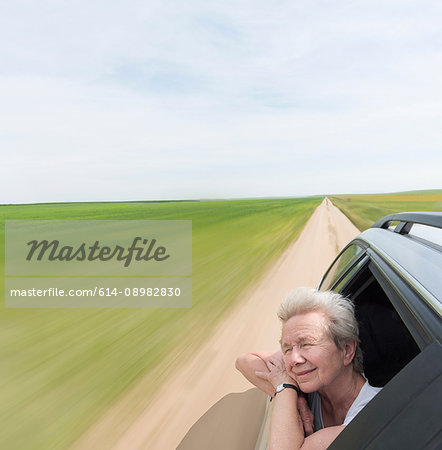 Senior woman leaning on car window enjoying wind in face