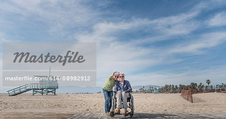 Senior man in wheelchair with wife pointing from beach, Santa Monica, California, USA