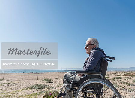 Senior man in wheelchair looking out from dunes, Playa del Ray, California, USA