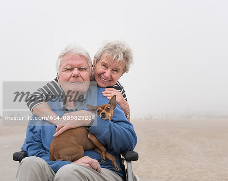 Portrait of senior man in wheelchair with wife and dog at beach, Santa Monica, California, USA