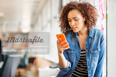 Female digital designer on office desk looking at smartphone