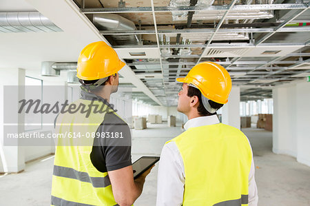 Two men wearing hi vis vest, having discussion in newly constructed office space, rear view