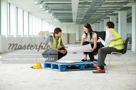 Three people sitting in newly constructed office space, looking at construction plans