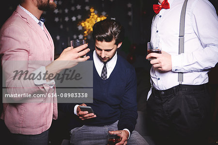 Three men at party, man in middle using smartphone