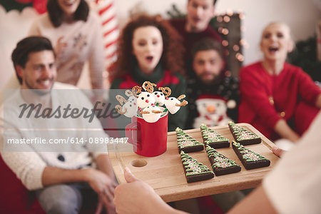 Over shoulder view of young woman serving friends with christmas biscuits at christmas party