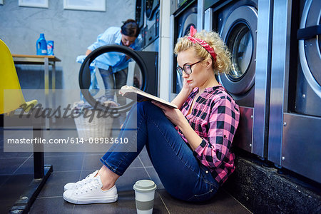 Woman sitting on laundrette floor reading book