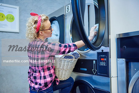 Woman removing laundry from tumble dryer in laundrette