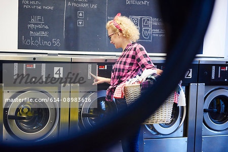 Woman pressing washing machine buttons at laundrette