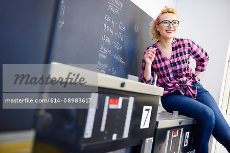 Female laundrette owner sitting on top of washing machine by chalkboard
