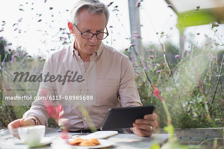 Senior man using digital tablet and drinking coffee at patio table