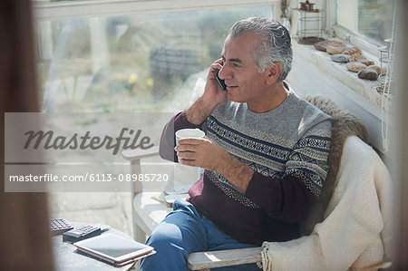 Senior man drinking coffee and talking on cell phone on sun porch