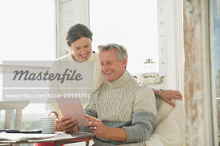 Smiling mature couple using digital tablet at table on sunny sun porch Smiling mature couple using digital tablet at table on sunny sun porch
