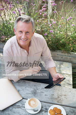 Portrait smiling senior man using digital tablet and drinking coffee at patio table