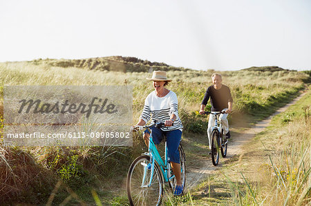 Mature couple riding bicycles on sunny beach grass path