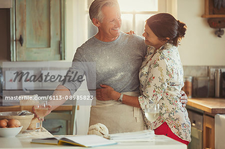 Affectionate mature couple hugging, baking and drinking wine in kitchen