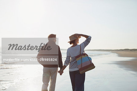 Affectionate mature couple holding hands and walking on sunny beach