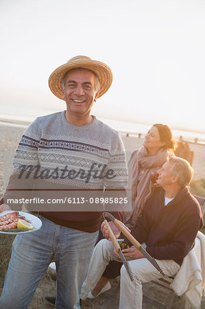 Portrait smiling senior man barbecuing with friends on sunset beach