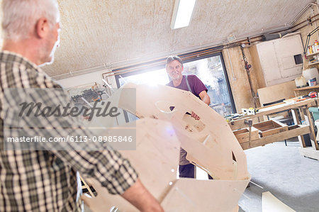 Male carpenters moving wood boat shell in workshop