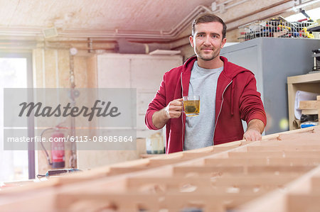 Portrait confident male carpenter drinking tea at wood boat in workshop