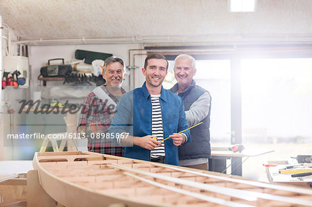 Portrait smiling male carpenters working at wood boat in workshop