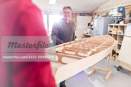 Smiling male carpenters moving boat in workshop