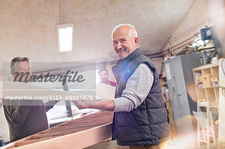 Portrait smiling senior male carpenter lifting wood boat in workshop