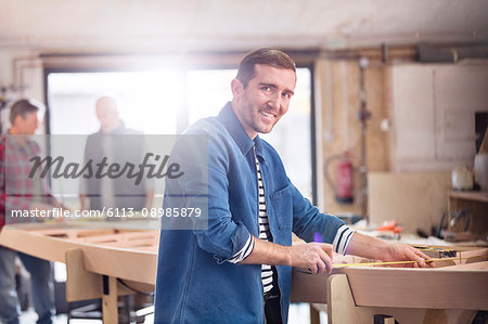 Portrait smiling male carpenter measuring wood on boat in workshop
