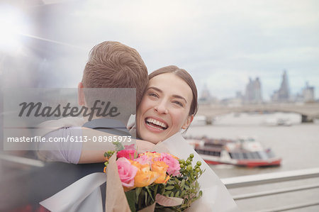 Happy, grateful woman receiving flower bouquet, hugging boyfriend on urban waterfront