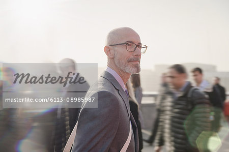 Serious, pensive businessman walking on busy urban pedestrian bridge