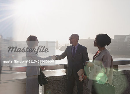 Silhouette business people handshaking on sunny urban bridge over Thames River, London, UK