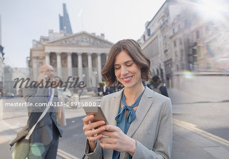 Businesswoman texting with cell phone on urban city street, London, UK