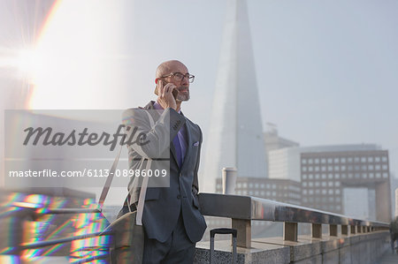 Businessman talking on cell phone on bridge, London, UK