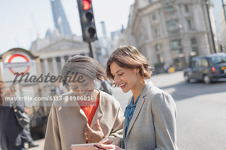Smiling businesswomen with digital tablet talking on sunny urban city street
