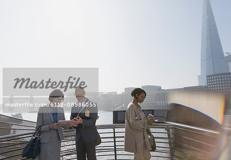 Business people using digital tablet at sunny urban waterfront, London, UK