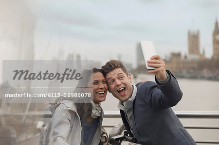 Playful couple tourists taking selfie with camera phone on bridge, London, UK