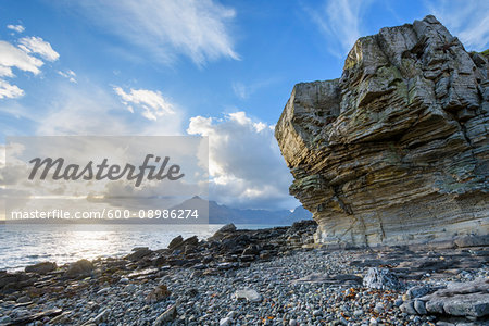 Rock face of sea cliff with honeycomb weathering and sun shining over Loch Scavaig on the Isle of Skye in Scotland, United Kingdom