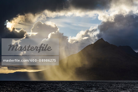 Sun breaking through the dramatic clouds along the Scottish coast over Loch Scavaig on the Isle of Skye in Scotland, United Kingdom