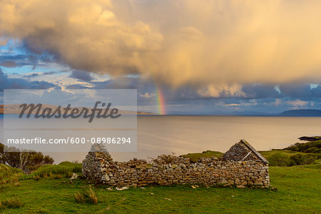 Remains of a stone house on the Isle of Skye with a rainbow appearing over the coast in Scotland, United Kingdom