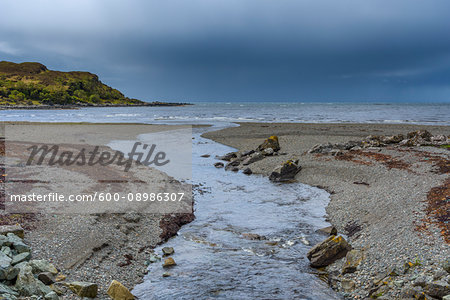 River flowing into sea bay with storm clouds over the ocean at the Isle of Skye in Scotland, United Kingdom
