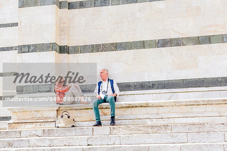 Tourist couple sitting on Siena cathedral stairway, Tuscany, Italy