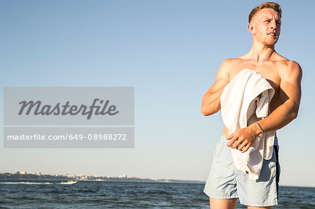 Young male swimmer drying himself with towel on beach