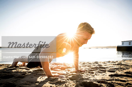 Young man training, doing push ups on sunlit beach