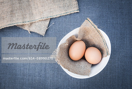 Two eggs on fabric, in bowl, overhead view